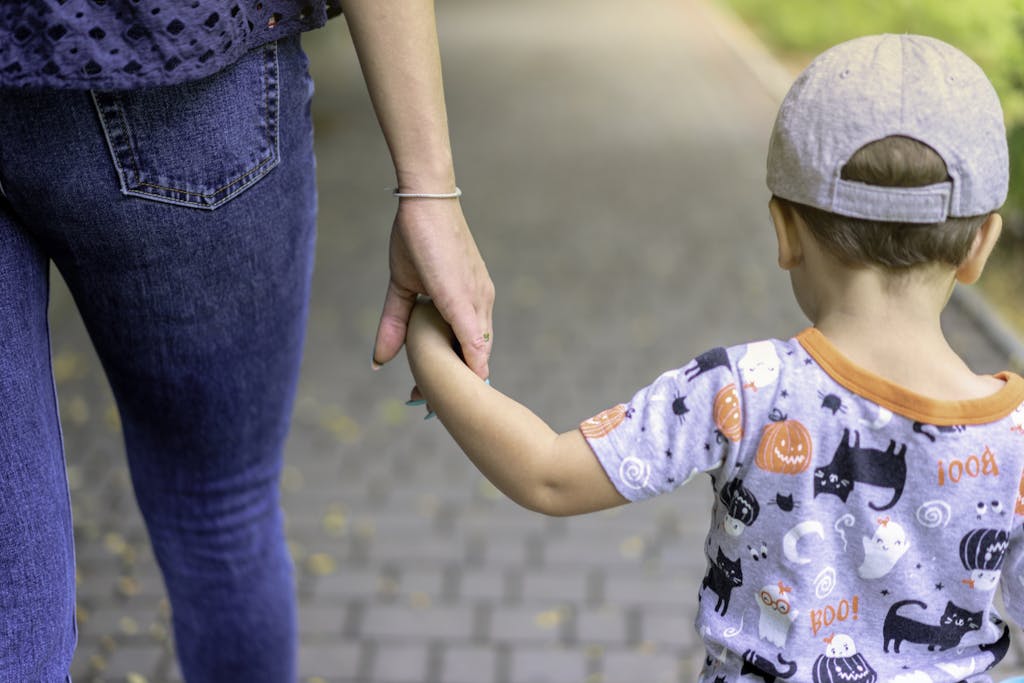 A mother and child enjoy a walk together holding hands on a sunny day.