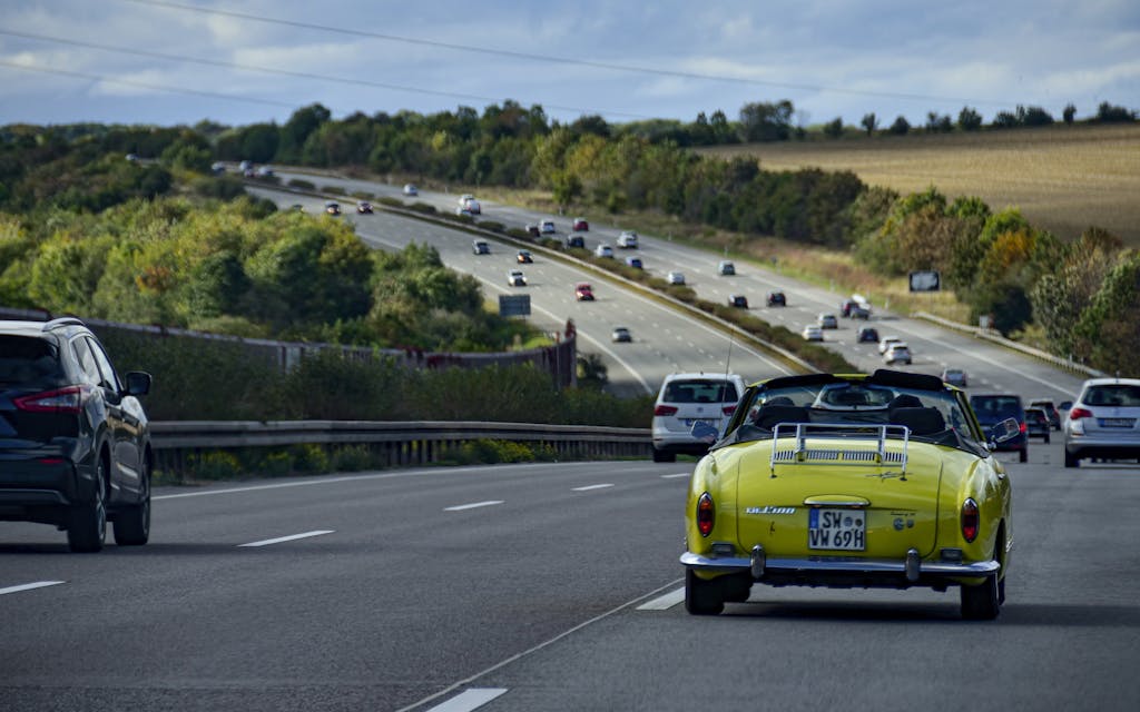 A vintage car travels on a German highway amid lush countryside scenery, highlighting automotive travel.