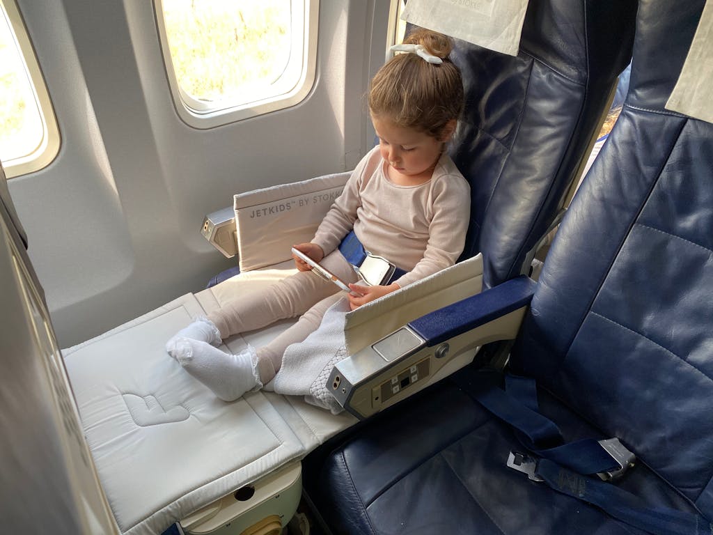 A young girl comfortably sitting in an airplane seat using her mobile device during flight.