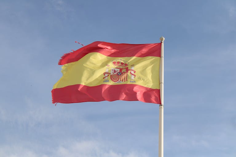 The Spanish flag flying against a clear sky in El Puerto de Santa María, Spain.