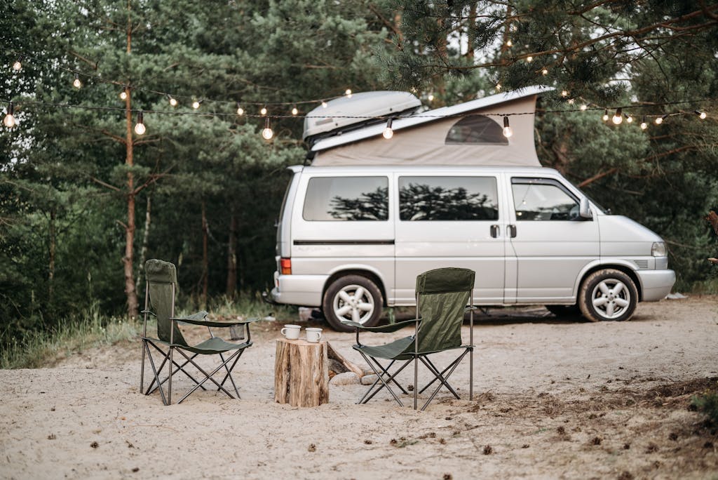 Tranquil forest campsite featuring a van, chairs, and string lights.