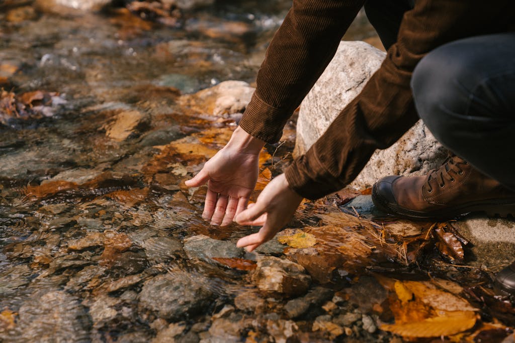 Side view of crop anonymous male in outerwear washing hands in water of lake with transparent water