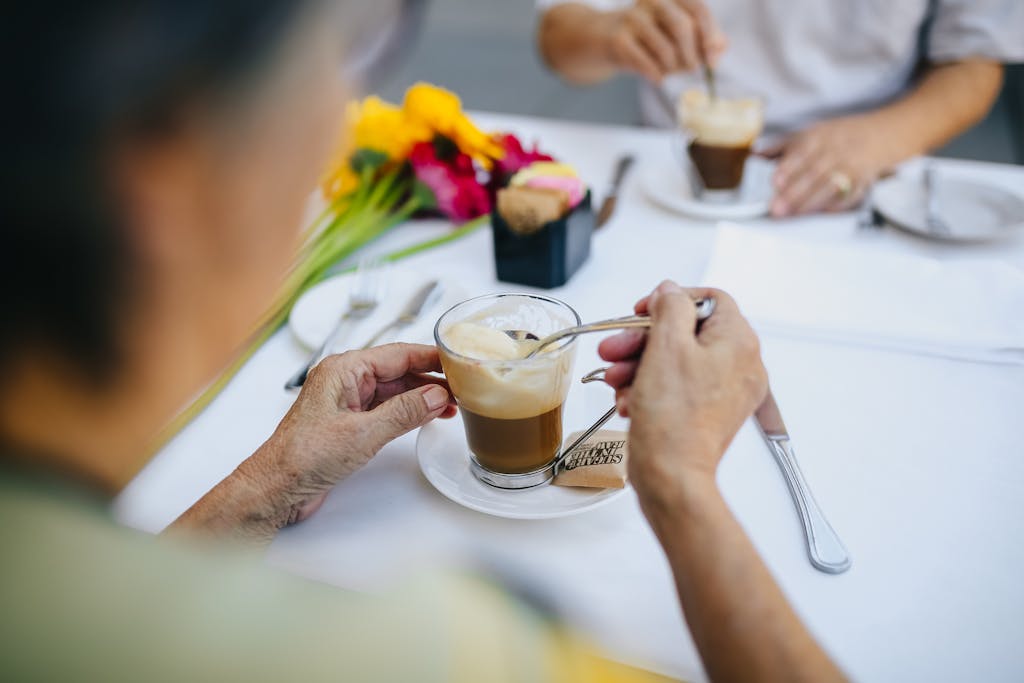 Senior couple stirring coffee at an outdoor cafe. Bright flower decor adds a cheerful touch.